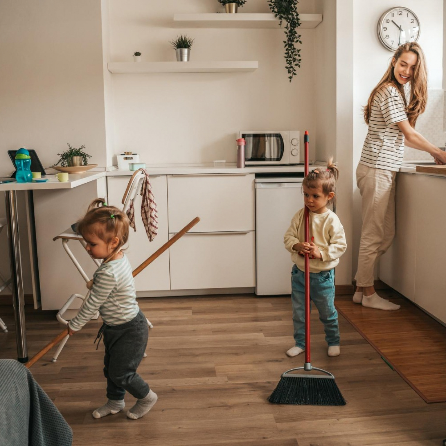 smiling-happy-young-mother-washing-dishes-watching-her-children-sweeping-floor-with-mops