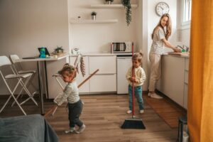 smiling-happy-young-mother-washing-dishes-watching-her-children-sweeping-floor-with-mops