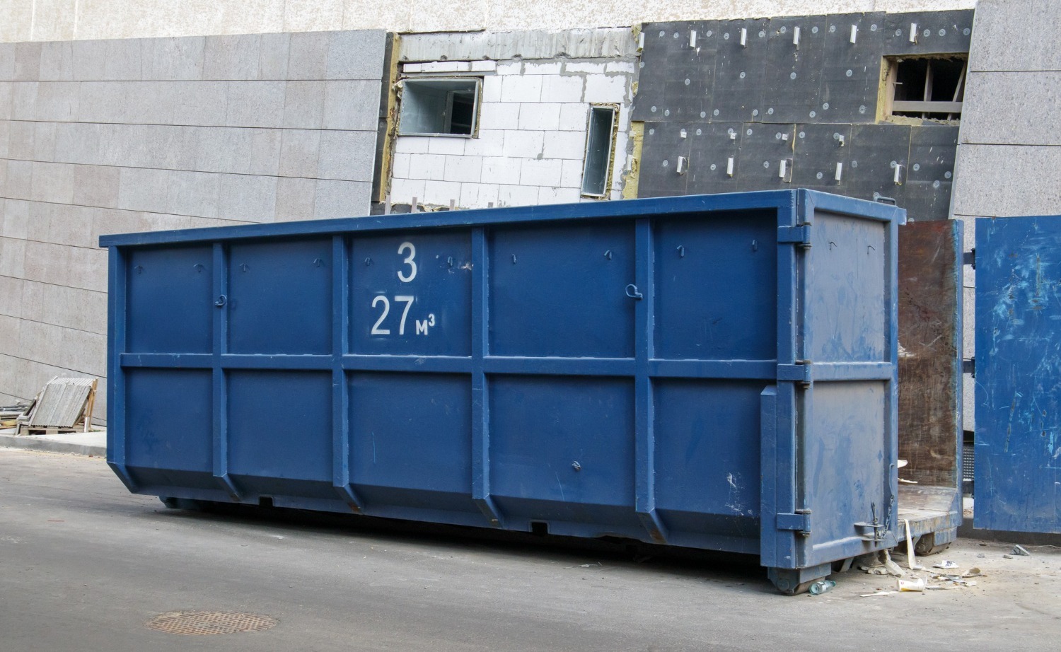 A blue garbage bin outside a construction site - for more information on efficient waste management, check out the Burlington Bin Rental FAQs
