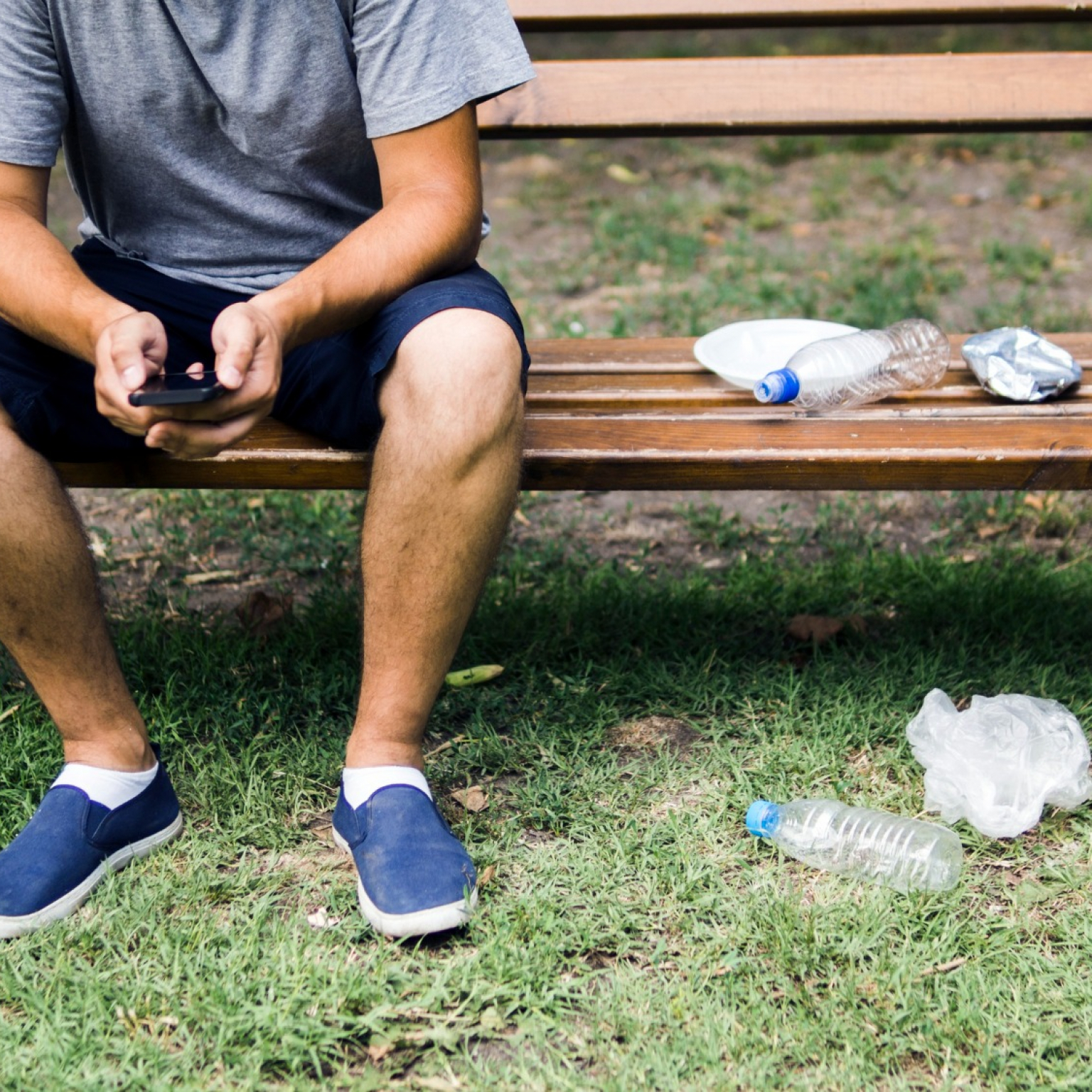 man-using-cellphone-sitting-bench-near-plastic-trash-park