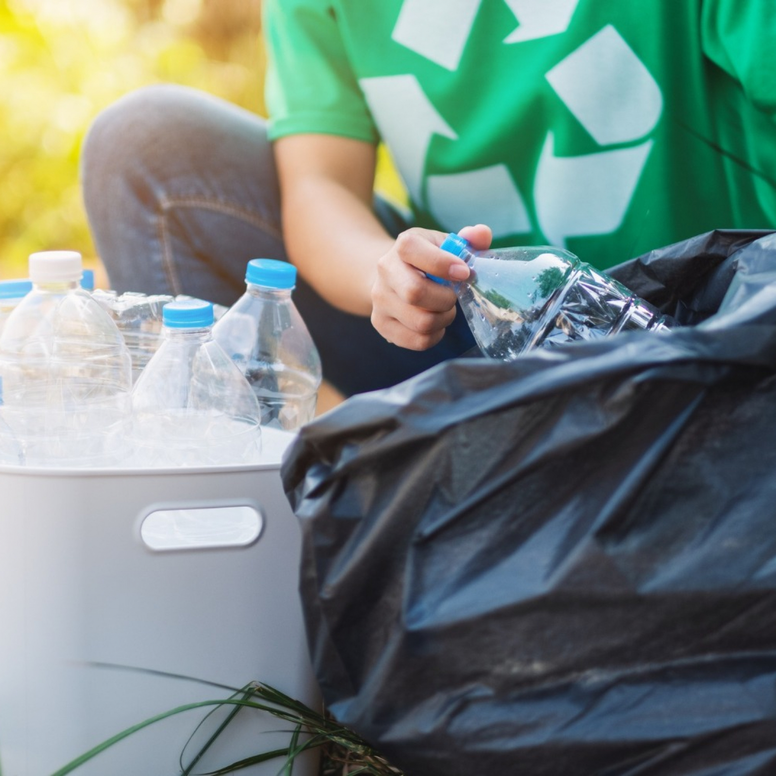 woman picking up garbage plastic bottles from the box into a plastic bag to promote a proper waste disposal