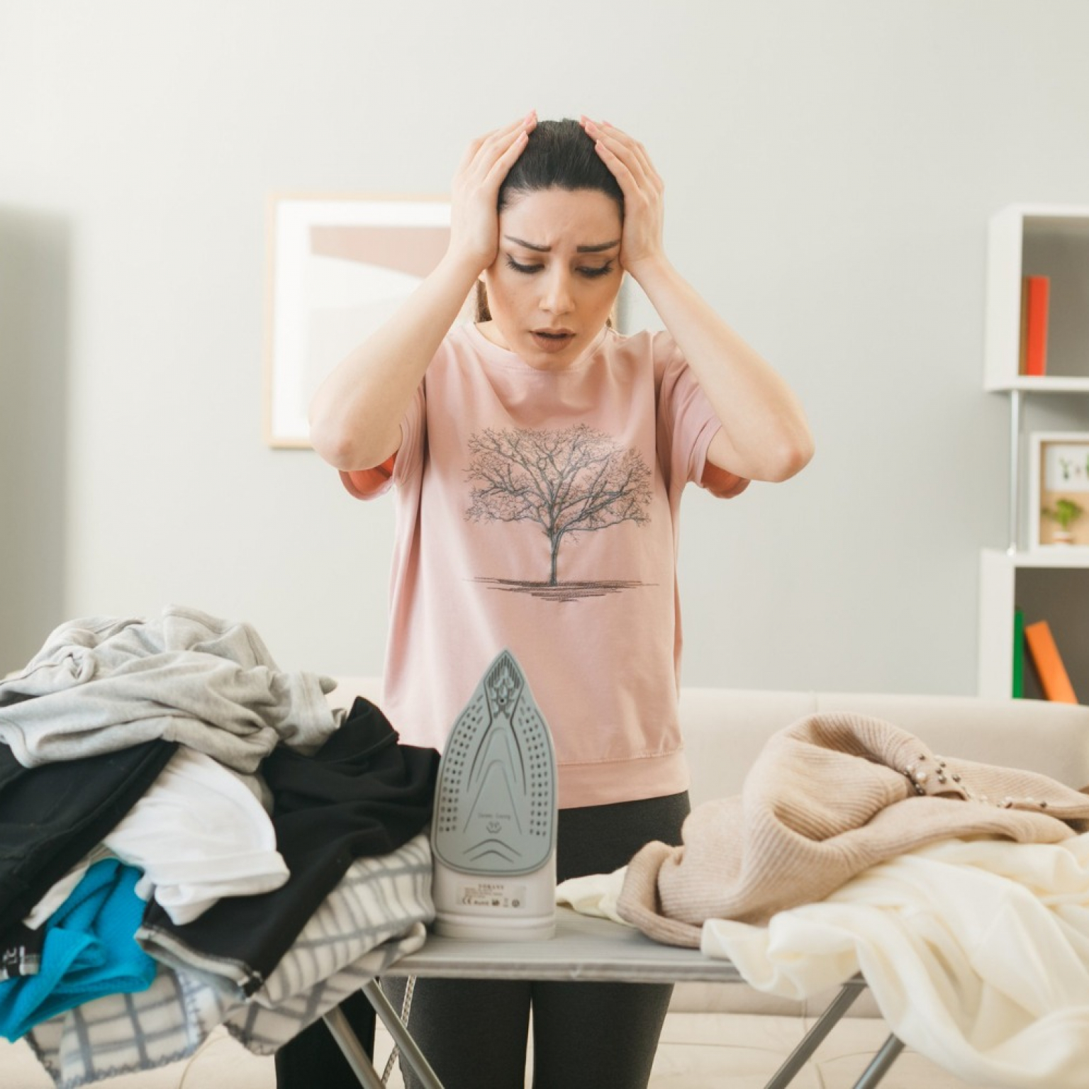 tired young woman house cleaner standing inside the living room going to iron the clothes on the ironing board