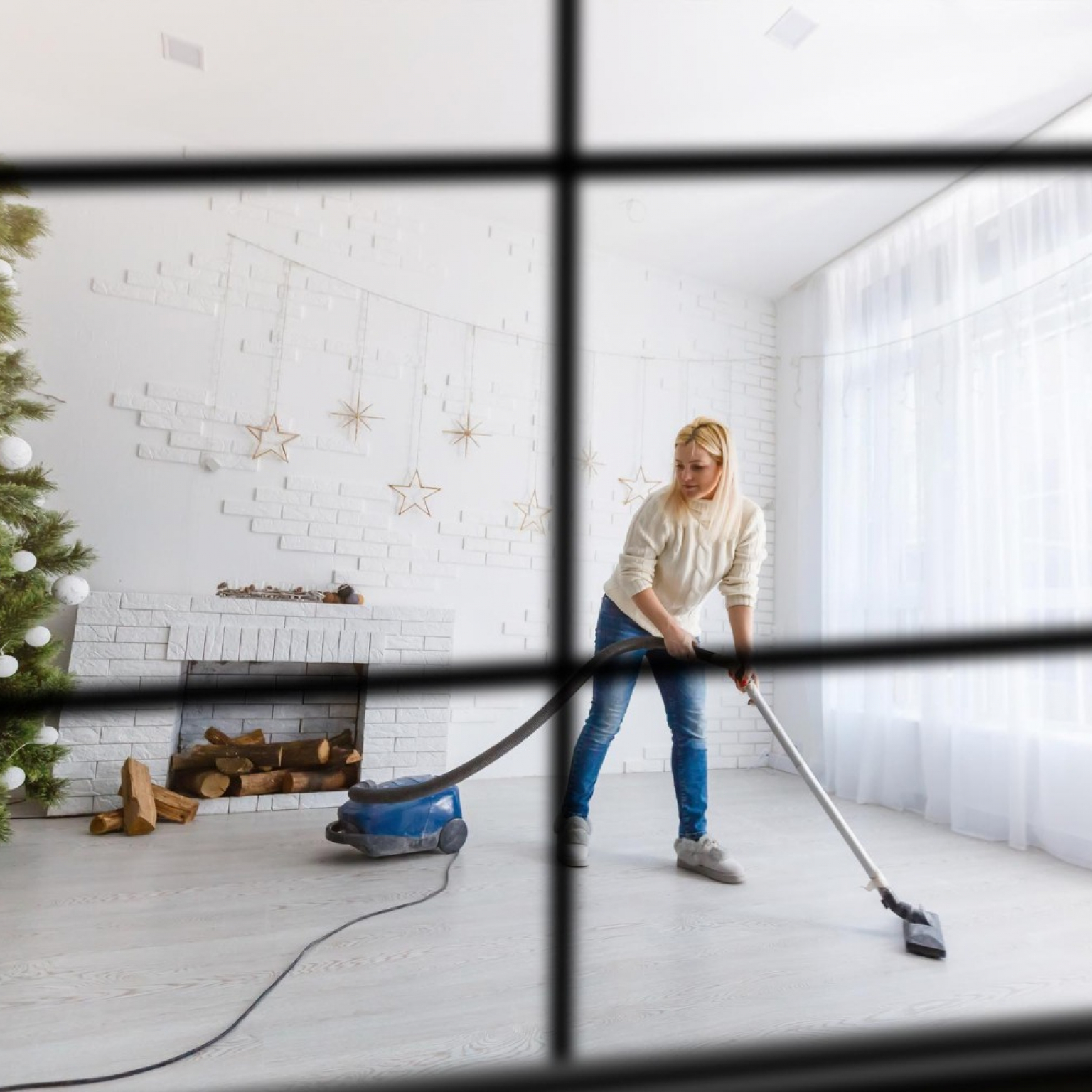 view through from a window a woman near a Christmas tree vacuuming the floor of her living room for a DIY cleaning