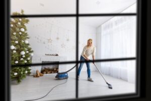 view through from a window a woman near a Christmas tree vacuuming the floor of her living room for a DIY cleaning