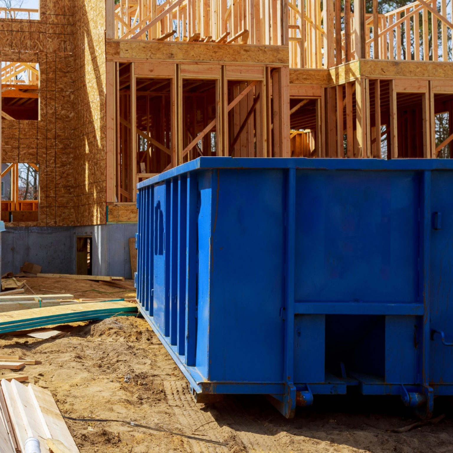 a rented blue Junk It garbage bin outside an ongoing house roof renovation to be used as garbage bin for the roof debris and other construction waste