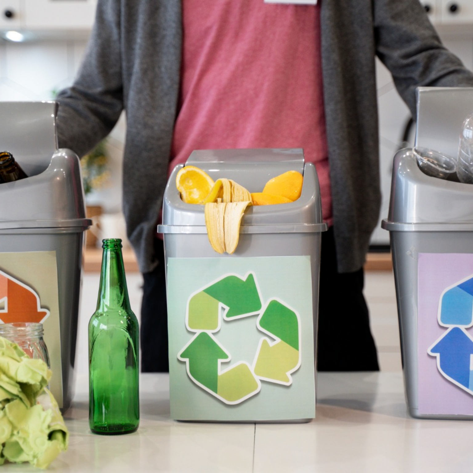 a person wearing a gray jacket with 3 kinds of trash bins properly sorting the household wastes