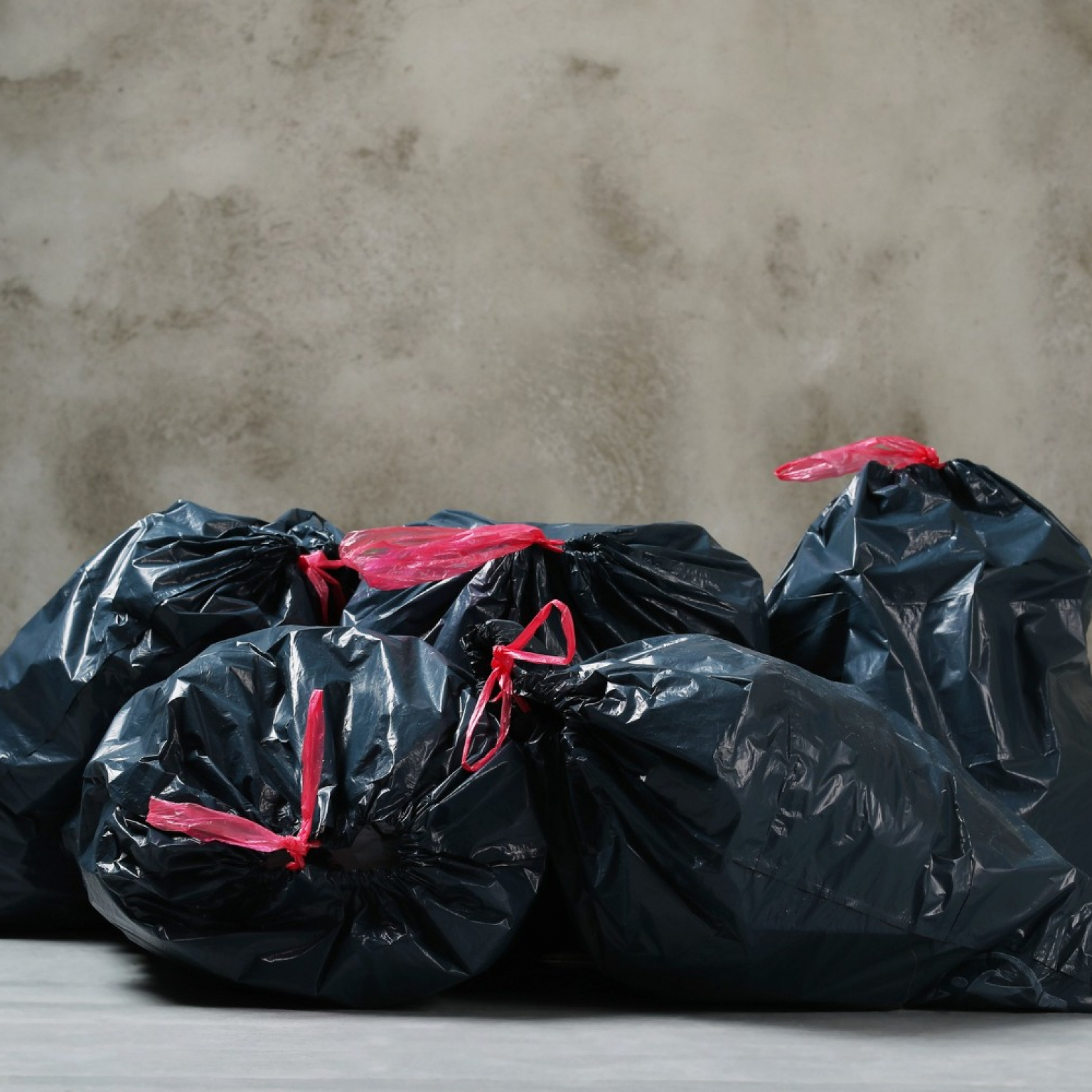 4 bags of trash being left behind near the wall a result of having trouble with dumpster bags
