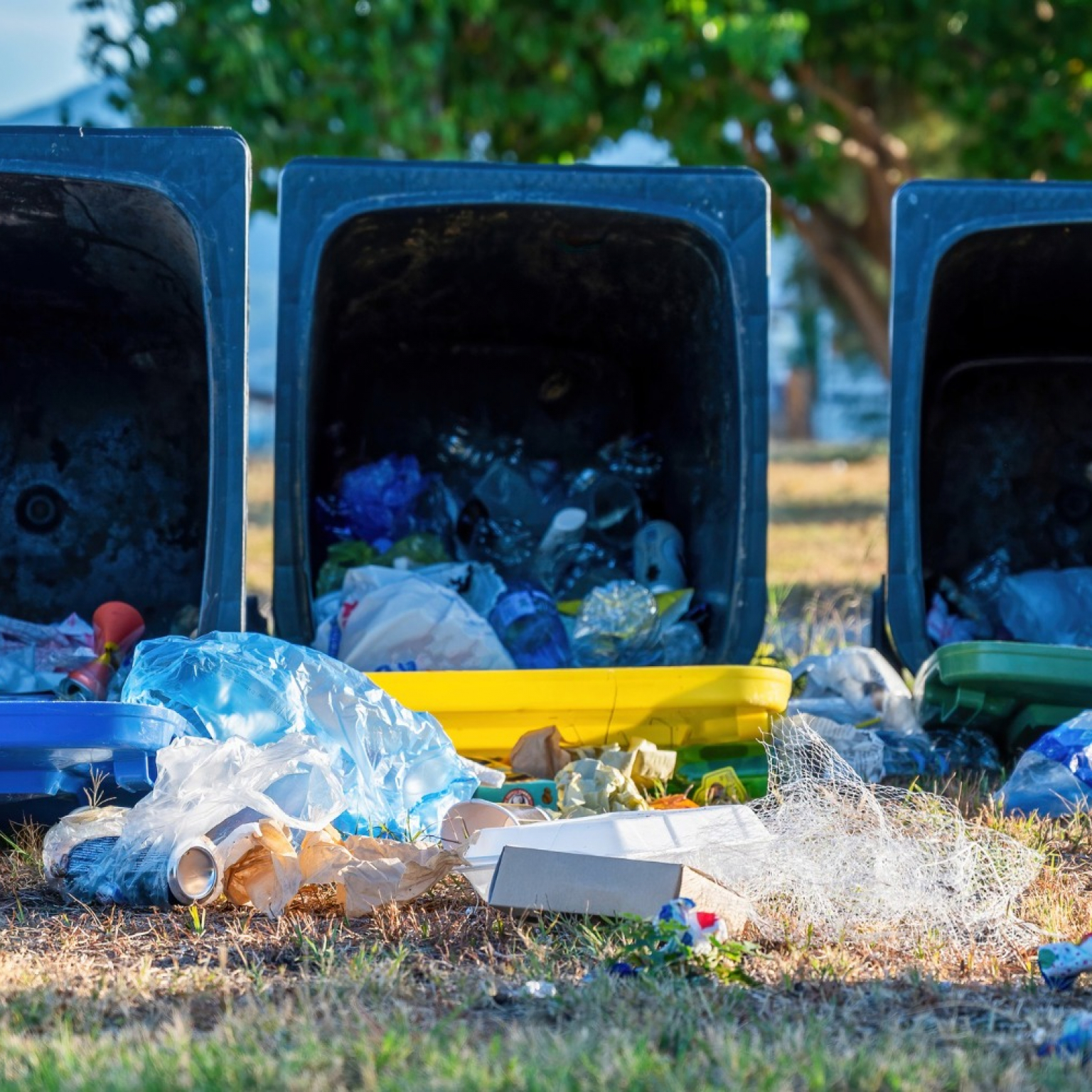 3 blue dropped Junk It recycling bin with fallen out trash on the ground being thought that can be put in the bin but can't