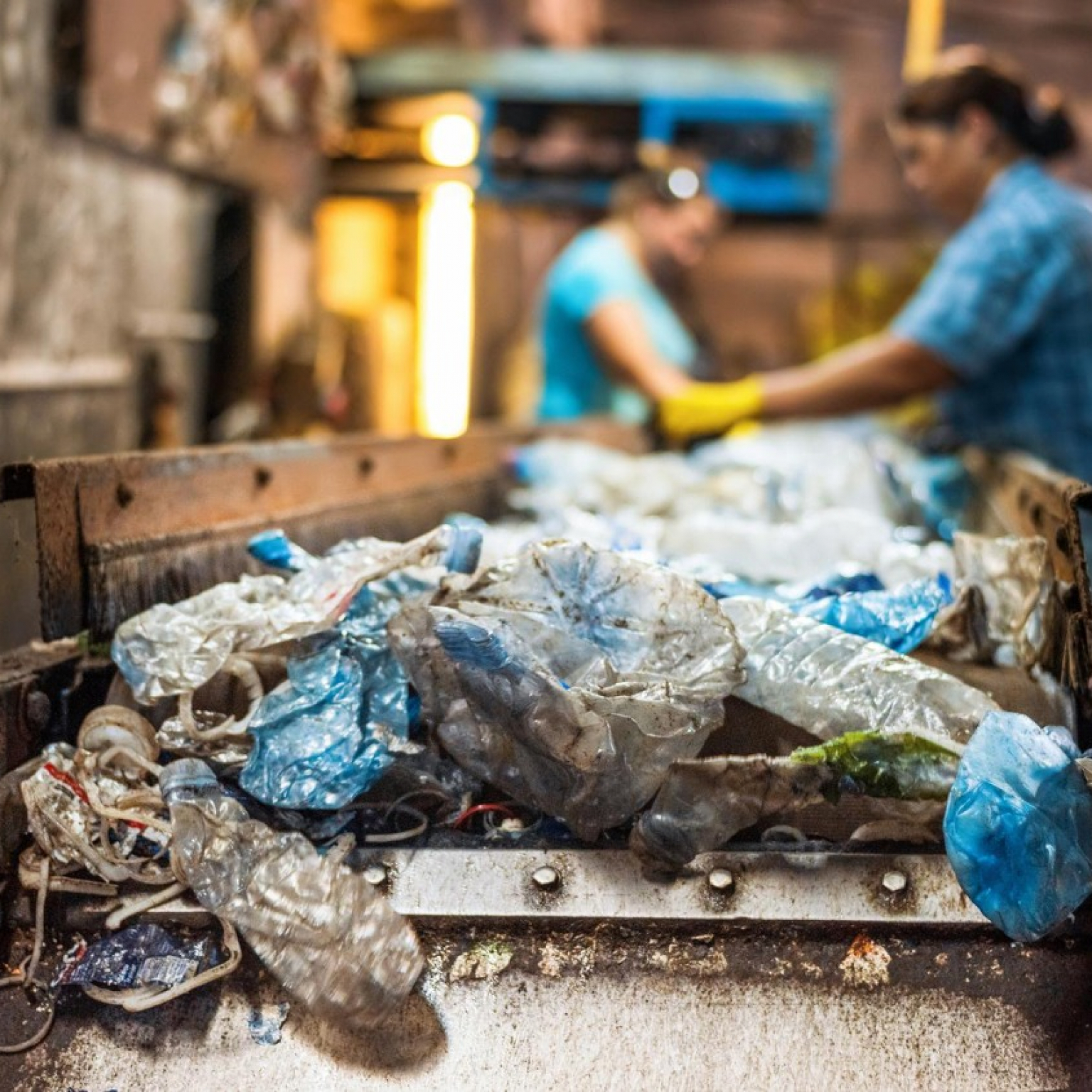 plastic garbage on a conveyor belt inside Junk It waste recycling facility with workers sorting recyclable materials