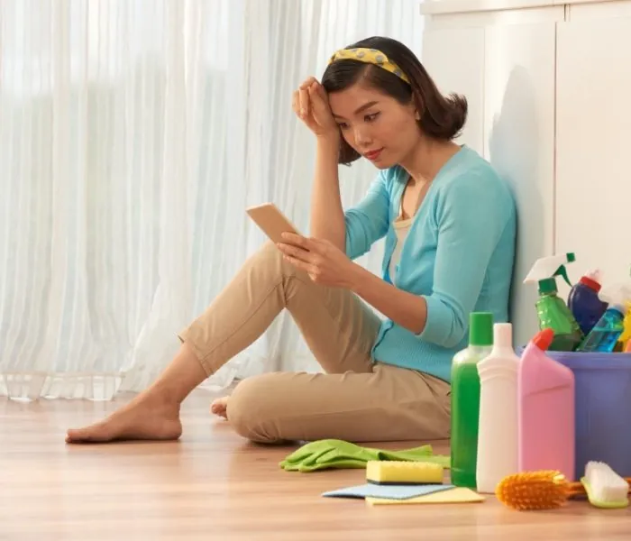 Woman checking her phone while surrounded by cleaning tools, planning to schedule a hassle-free garbage bin rental in Scarborough