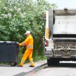 a Junk It bin rental service staff pulling a garbage bin into the dumpster truck