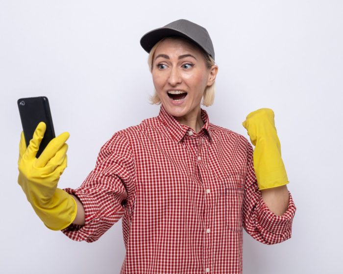 Smiling cleaning woman wearing gloves and happily browsing her phone - reflecting the convenience of garbage bin rental services in Hamilton for hassle-free cleanup solutions