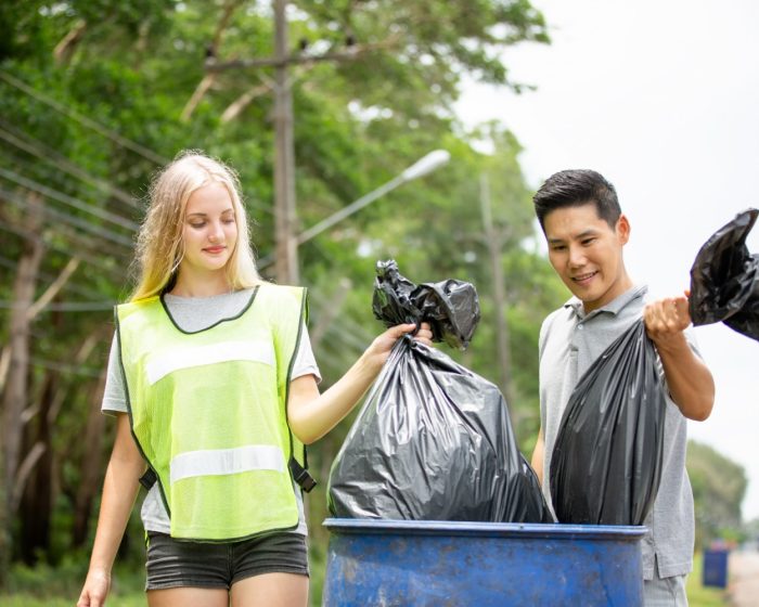 Two optimistic volunteers holding a garbage bag, helping to pick up trash, with information on Junk It’s dumpster rental services in Canada FAQs