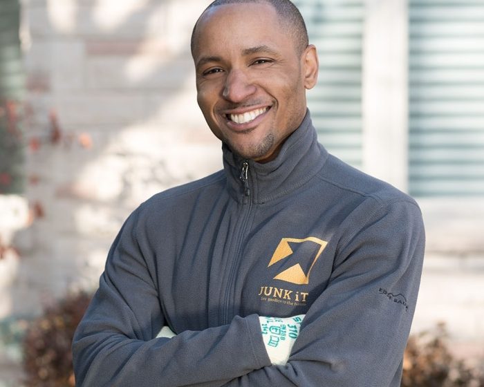A Black man, a Junk It employee smiling in a grey Junk It jacket, ready to help with your garbage bin rental in London, Ontario for efficient waste removal