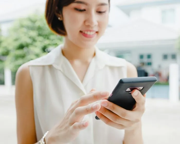 Woman in a white dress looking at her black phone - considering how garbage bin rental in Richmond Hill can help with her upcoming cleanup project