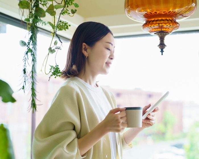 A woman holding a cup while looking at her phone - potentially researching garbage bin rental in London, Ontario for her next cleanup