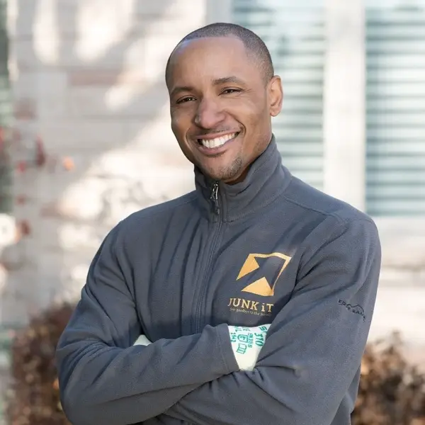 a Black man / junk it employee smiling in a grey Junk It jacket - junk it happy to serve you for dumpster rental needs in Hamilton