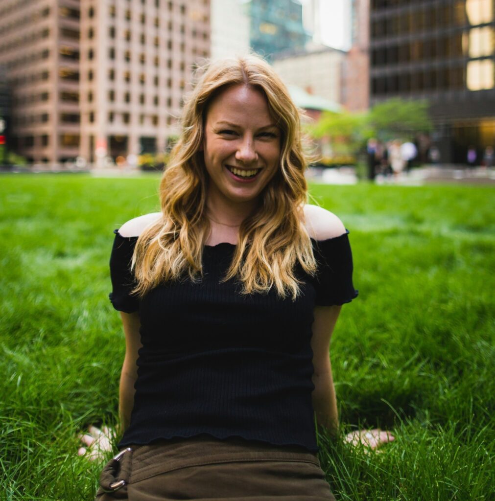 Blonde woman smiling in a black off-shoulder outfit, enjoying her day while thinking about the convenience of garbage bin rental in Toronto for her upcoming home clean-up.