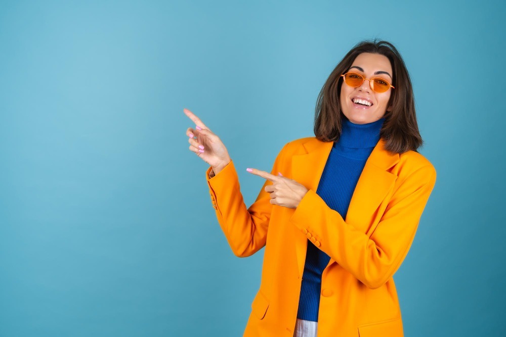 A woman wearing an orange blazer is pointing to her left - showcasing Dumpster Bin Rentals with Junk It