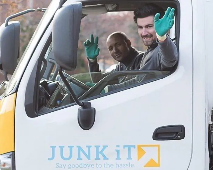 two Junk It employees waving inside a truck - ready to assist with your garbage removal needs through trusted garbage bin rental in North York