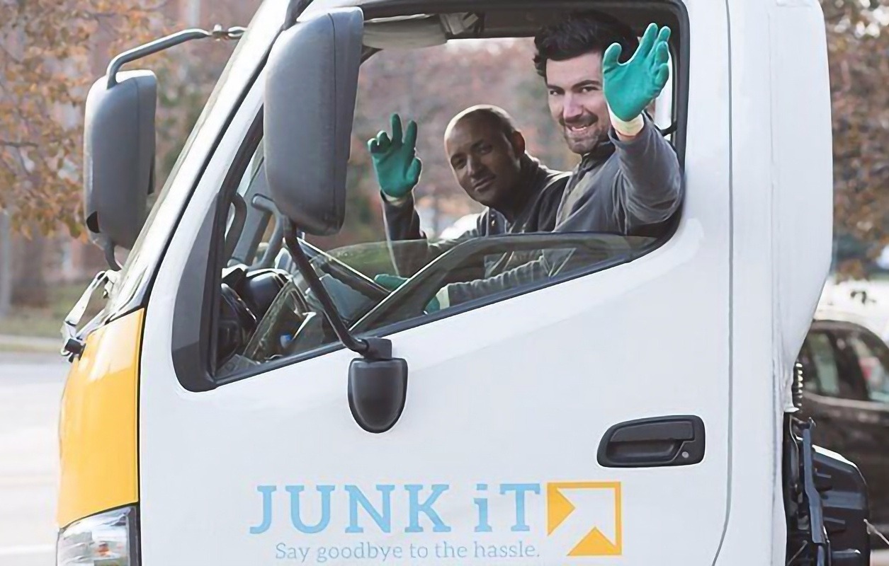 two junk it employees waving inside a truck - learn more about junk it - Reliable Bin and Dumpster Rental Services Across Canada