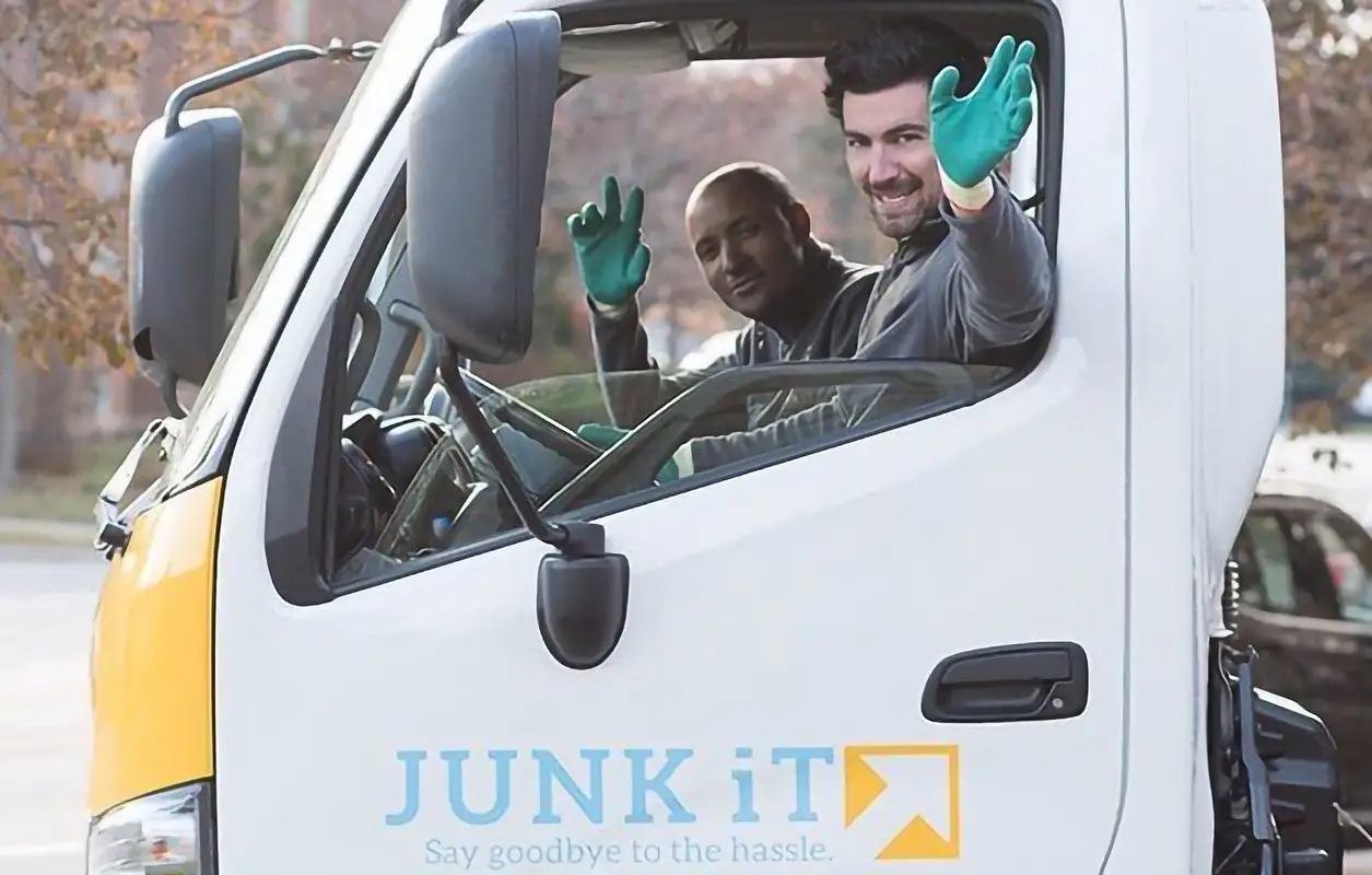 two junk it employees waving inside a truck - learn more about junk it - Reliable Bin and Dumpster Rental Services in Edmonton