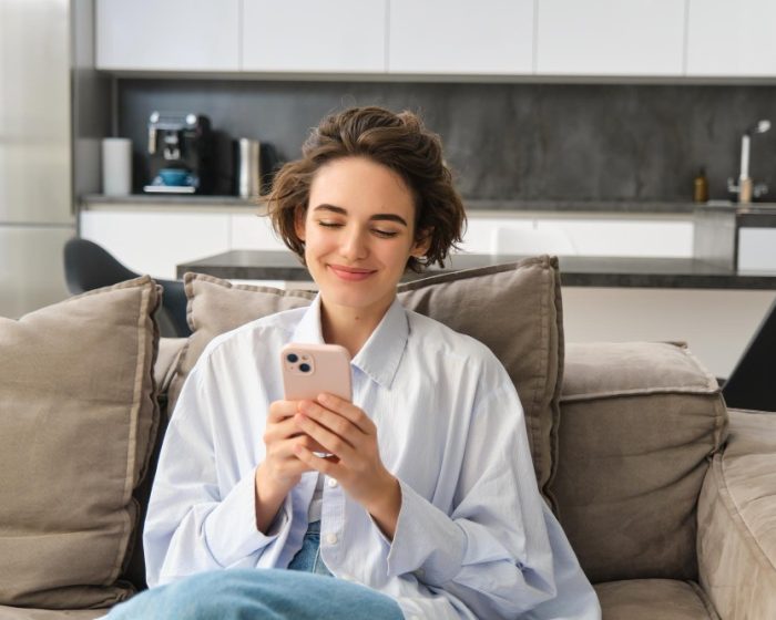 A woman sitting on a couch using her phone - exploring options for garbage bin rental in London, Ontario to manage home cleanup
