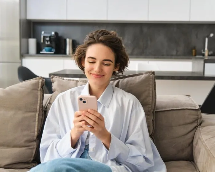 A woman sitting comfortably while looking at her phone - considering garbage bin rental in Milton for her next decluttering project