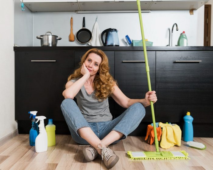 A woman sitting on the floor while holding a green mop - thinking about organizing and cleaning up - with options for garbage bin rental in Milton to help with decluttering