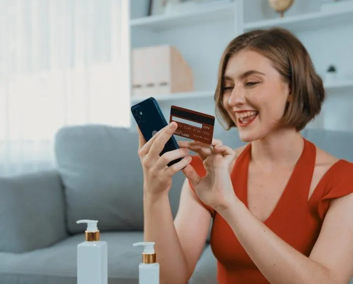 A woman in a red shirt smiling as she holds her phone and card - considering the convenience of garbage bin rental in Vancouver for her upcoming home renovation project