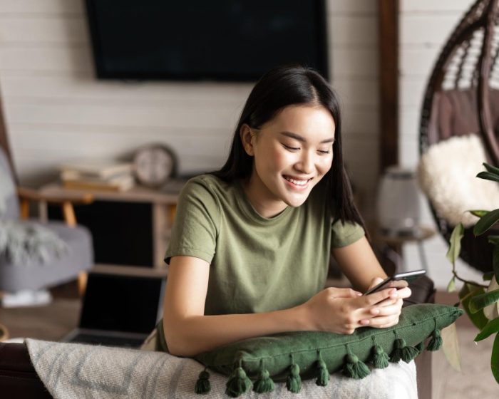an Asian woman wearing a green shirt smiling at her phone, exploring convenient garbage bin rental in North York to simplify her cleanup plans